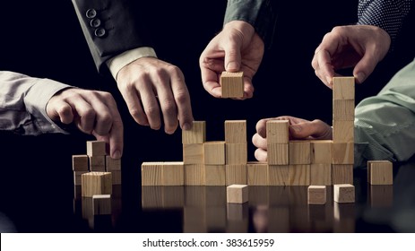 Teamwork and cooperation concept - five male hands building a structure of wooden blocks on black desk with reflection, toned retro effect.