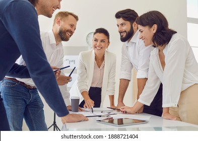 Teamwork And Cooperation Concept. Group Of Young Smiling Business People Standing Over Table And Discussing New Project Or Startup Idea During Meeting Together