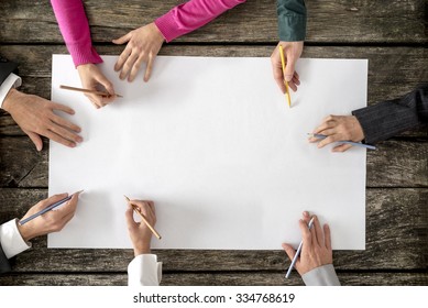 Teamwork and cooperation concept - top view of six people - men and women - drawing or writing on a large white blank sheet of paper. - Shutterstock ID 334768619