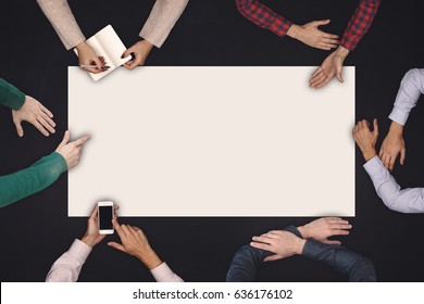 Teamwork and cooperation concept - top view of six people drawing or writing on a large white blank sheet of paper on blackboard.