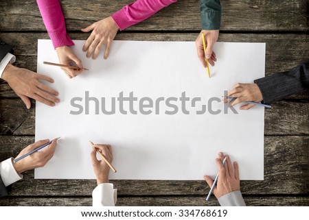 Teamwork and cooperation concept - top view of six people - men and women - drawing or writing on a large white blank sheet of paper.