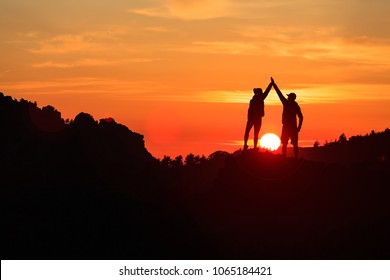 Teamwork couple celebrating silhouette in inspiring mountains sunset. Team of climbers celebrate reached goal and success. Achievement and motivation concept on top of mountain, Corsica France.