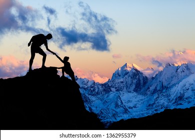 Teamwork Couple Helping Hand, Trust In Mountains. Team Of Climbers Man And Woman Hiking, Help Each Other On Top Of Mountain, Climbing Together, Inspiring Sunset On Elbrus, Russia.