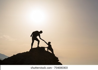 Teamwork Couple Helping Hand Trust Silhouette In Inspiring Mountains. Team Of Climbers Assistance Man And Woman Hiker, Help Each Other On Top Of Mountain, Beautiful Sunrise Landscape In Crete Greece