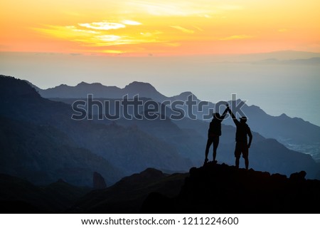 Teamwork couple helping hand trust help, silhouette success in mountains. Team of climbers man and woman. Hikers celebrate with hands up, help each other on top of mountain, sunset landscape.