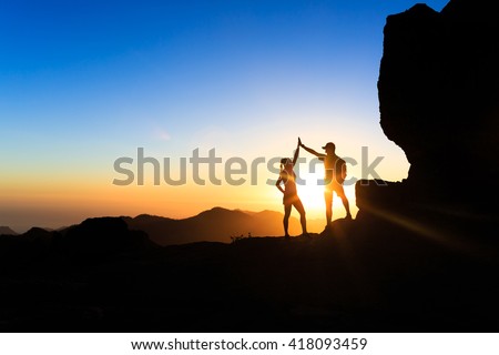 Teamwork couple helping hand trust help, silhouette success in mountains. Team of climbers man and woman. Hikers celebrate with hands up, help each other on top of mountain, happy climbing together.