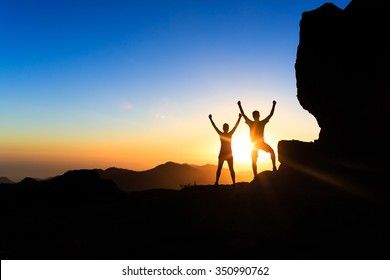 Teamwork couple hikers success in sunset mountains, accomplish with arms up outstretched. Young man and woman on rocky mountain range looking at beautiful inspirational landscape view, Gran Canaria. - Shutterstock ID 350990762