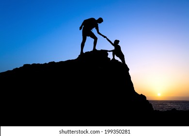 Teamwork Couple Hiking Help Each Other Trust Assistance Silhouette In Mountains, Sunset. Teamwork Male And Woman Hiker Helping Each Other On Top Of Mountain Climbing Team, Beautiful Sunset Landscape.