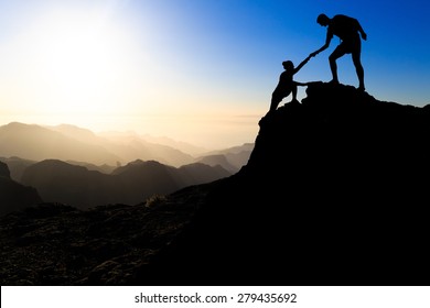 Teamwork Couple Hiking Help Each Other Trust Assistance Silhouette In Mountains, Sunset. Team Of Climbers Man And Woman Hiker Helping Each Other On Top Of Mountain, Climbing Trust Beautiful Landscape.