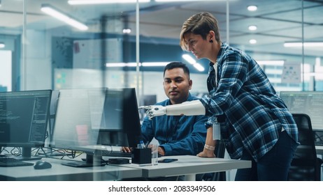 Teamwork In Diverse Inclusive Office: Woman With Disability Project Manager With Prosthetic Arm Talks With Indian Specialist Working On Desktop Computer. Professionals Software Engineers Create App