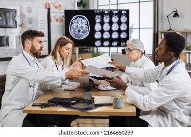 Teamwork Of Diverse Neuroscientists Sharing Lists With Researchings While Discussing Disease Problems In Science Laboratory. Healthcare Workers Using Monitor With X Ray Scan Showing Brain Anomalies.