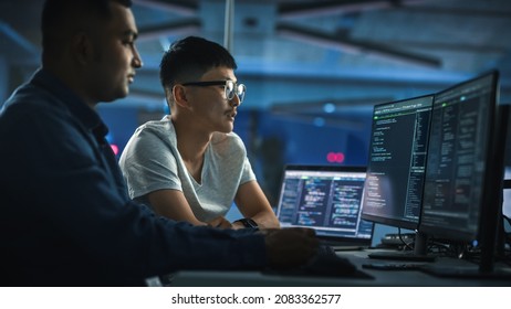 Teamwork In Diverse Office at Night: Project Manager Talks with Creative Solutions Specialist, They Discuss App Code Computer. Stylish Professionals Programming, Create e-Commerce Software - Powered by Shutterstock