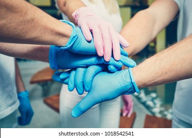 Teamwork Of The Doctors In Hospital. Hands Of Four Men In Blue Gloves And One Woman In Pink Gloves. Themes Health Care, Cooperation, Trust And Success. 