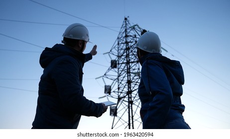 Teamwork And Engineers, Partners Shaking Hands, Good Work. Power Workers In Protective White Helmets Are Checking Power Line Online Using Computer Tablet. Business Concept. Woman And Man Work Together