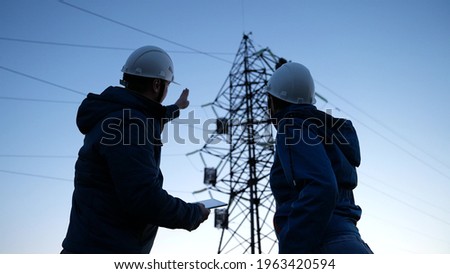 Teamwork and engineers, partners shaking hands, good work. Power workers in protective white helmets are checking power line online using computer tablet. Business concept. Woman and man work together