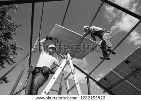 Teamwork for installing innovative solar pannels on the roof for using renewable energy resources. Envirinment friendly green energy. Economical, innovative solution for housebuilding. Black and white