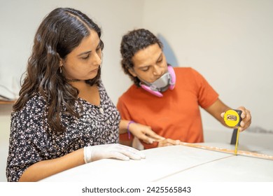 Teamwork measuring a piece of a surfboard using a tape in a workshop - Powered by Shutterstock