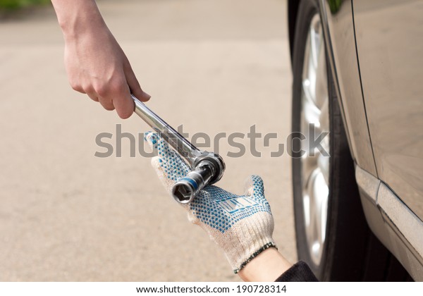 Teamwork as a mechanic\
fixing a car that has broken down at the side of a road is handed a\
steel socket wrench spanner by the female driver, close up view of\
their hands