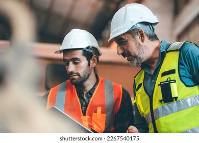 Teamwork men in construction site, Two civil engineer or professional foreman in safety helmet hard hat using blueprint in digital tablet working while standing at industrial factory, teamwork concept