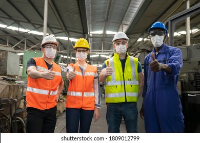 Teamwork of multiethnic engineer with workers giving thumbs up and wearing surgical mask to prevent covid-19 in manufacturing factory. Concept of race and gender equality in workplace.
