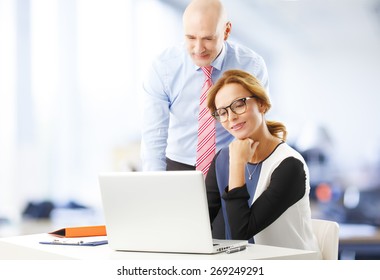 Teamwork At Office. Portrait Of Middle Age Businesswoman And Senior Businessman Sitting At Desk In Front Of Computer And Working On Presentation. At Background Sitting Business Persons. 