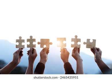 Teamwork and partnership concept. Hands are raised against a bright, white sky, each holding a piece of a wooden jigsaw puzzle. teamwork, problem-solving, Charity, volunteer. Unity, team business. - Powered by Shutterstock