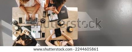 Teamwork in a small business team of women entrepreneurs discusses startup ideas. Top view of four women sitting around table in cafe with laptop, digital tablet and documents. Group of women working 