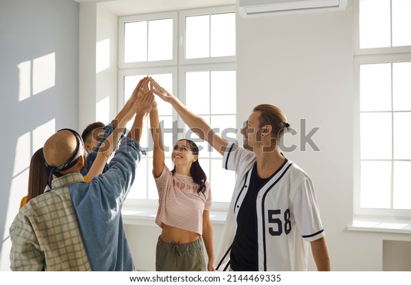 Teamwork spirit. Group of young hip hop
dancers raises their team spirit in preparation for dance
competitions. Smiling people raise and join hands. Concept of
respect, trust, support and
friendship.