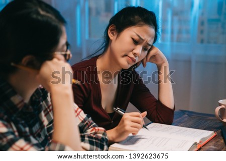 teamwork thinking brainstorming concept. two young college girls classmates working together at late night at home. frowning asian women friends consider about mathematics problem prepare for test