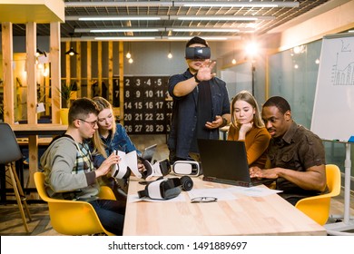 Teamwork Trying Virtual Reality Glasses For Work In Creative Office. Young Asian Man Using New Technology Vr Goggles While His Coworkers Talking Sitting At The Table