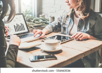 Teamwork. Two Young Business Woman Sitting At Table In Coffee Shop, Look At Chart On Laptop Screen And Develop Business Plan. Business Meeting In Restaurant. On Table Tablet PC,cup Of Coffee,notebook.