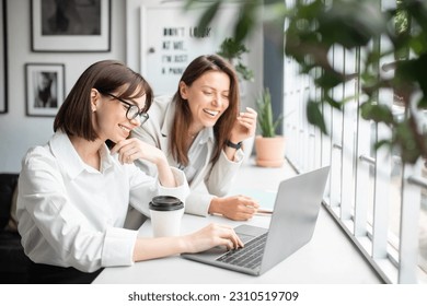 Teamwork and unity. Two young women specialists working together on laptop, discussign ideas and boosting productivity through corporate collaboration in office