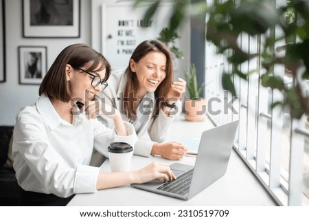 Teamwork and unity. Two young women specialists working together on laptop, discussign ideas and boosting productivity through corporate collaboration in office