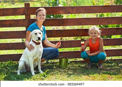 Teamwork - Woman With Little Girl And Dog Painting A Fence In Summer Time