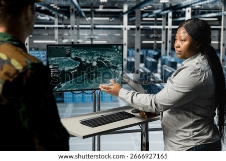 Teamworking army experts in data center confirming target locations using aerial image overlay on monitor. Military units in server room gathering strategic terrain data via satellite systems