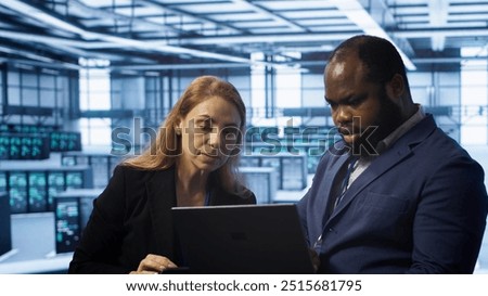 Teamworking colleagues in server farm using laptop to patch network issues affecting transfer rates. Coworkers in data center doing brainstorming, fixing errors affecting supercomputers, camera A
