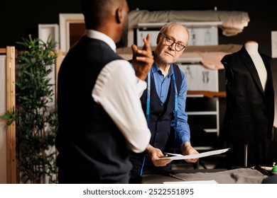 Teamworking fashion designers brainstorming upcoming sartorial luxury attire collection using sketches. Elderly suitmaker and apprentice trying to come up with creative ideas for bespoke clothing - Powered by Shutterstock