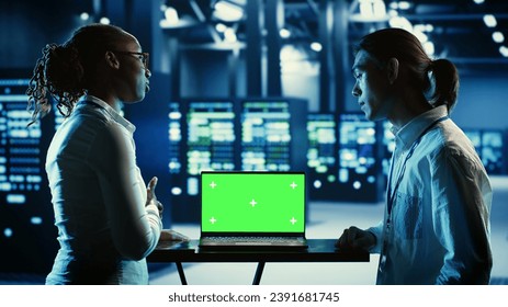 Teamworking professionals running code on chroma key laptop, troubleshooting data center equipment. Tech support executives using green screen device to monitor servers and networking systems
