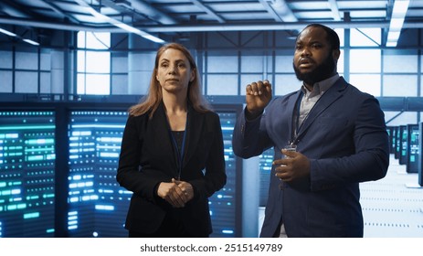 Teamworking technicians in high tech data center workspace looking at hologram visualization. Programmer and colleague working on securing server room hardware using AR tech, camera A