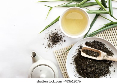 teapot and cup of herbal green tea on bamboo with white table background. over light
