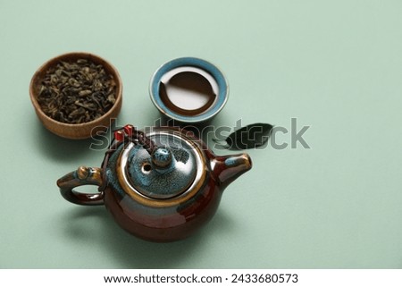 Teapot, cup of tea and bowl with dry leaves on olive background