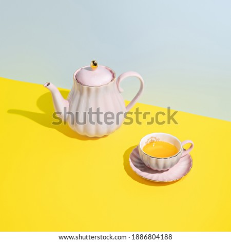 Teapot with cup of tea on multi colored pastel blue and yellow background. Minimal herbal organic beverage concept. Trend shadows.
