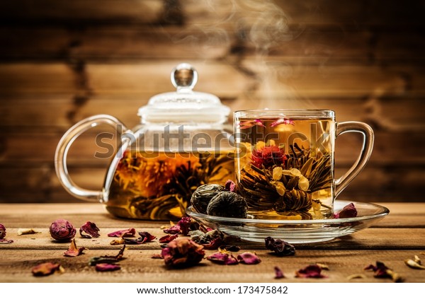 Teapot and glass cup with blooming tea flower\
inside against wooden background\
