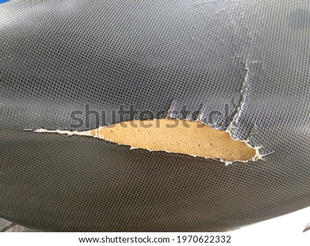 Tear marks at the seams until the sponge texture is visible. closeup of old and torn leather motorcycle seat, Old black leather surface texture background.