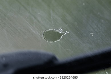 A teardrop ring marks the glass while a dark wiper edge crosses the frame. Scratches and soft green light complete the scene. The quiet composition suggests travel in gentle rain.