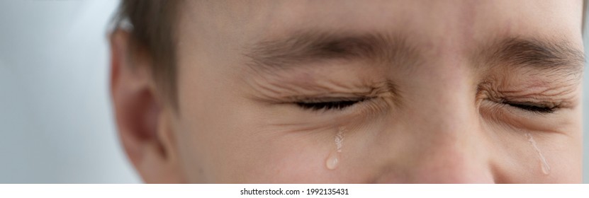 Teardrops rolls down the boy's cheeks, his eyes are closed, he is upset and crying. Sad, unhappy emotions of child, banner size.