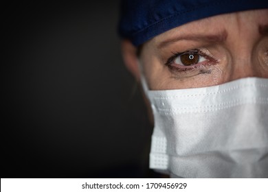 Tearful Stressed Female Doctor or Nurse Wearing Medical Face Mask on Dark Background.
