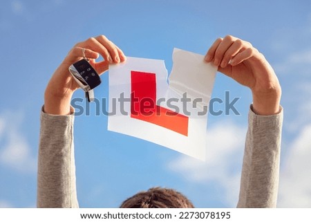 Tearing L plate against a sky holding a car key after passing driving test