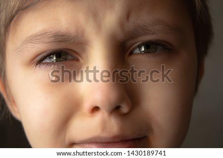 Tears in the eyes of a child. The boy is crying and a tear runs down his cheek. Close-up.