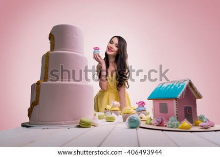Teasing people with her bakery to make them jelous. Beautiful smile of brunette. Always being positive and happy. Various confection on white wooden table.